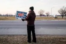 Person holding a sign that says "Execution is not the solution" while standing on the side of the road